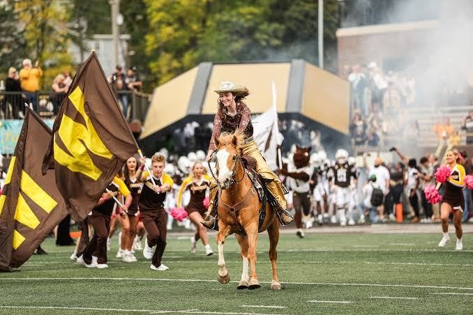 Western Michigan University rider on horseback leading flag bearers and cheerleaders onto the field